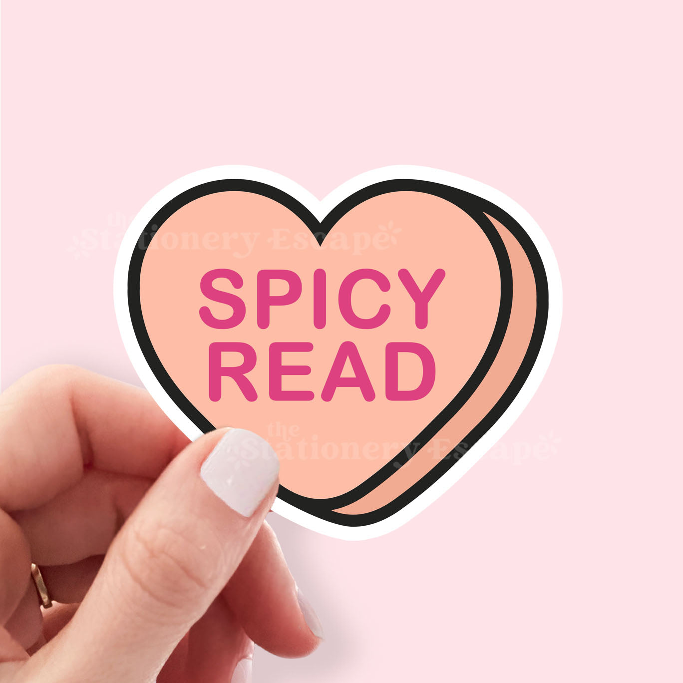 Heart-shaped sticker with 'SPICY READ' text held by a hand on a pink background