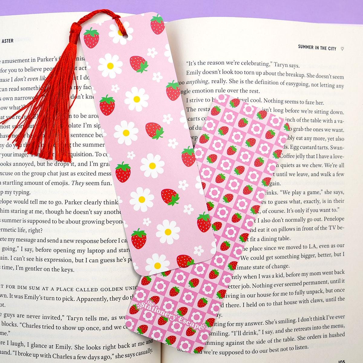 Pink strawberry-themed bookmark with a red tassel on an open book.