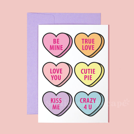 Greeting card with colorful heart-shaped "candies" and conversation heart text on a pink background