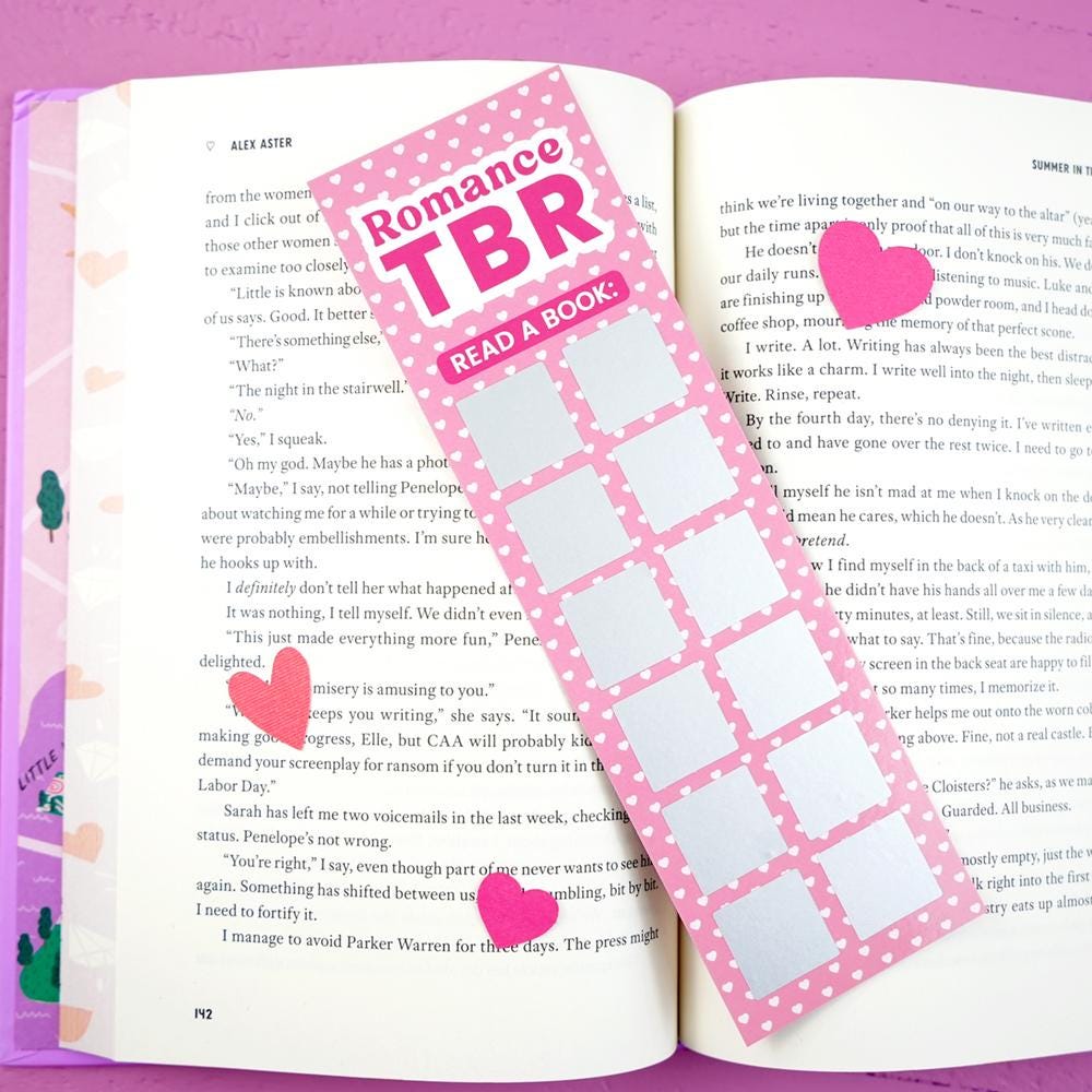 Open book with a pink 'Romance TBR' bookmark and heart stickers on a pink background