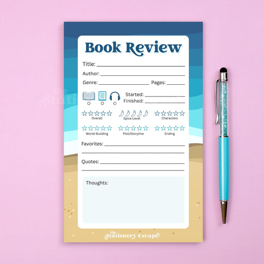 Blue and tan beach-themed book review notepad with a pen on a pink background