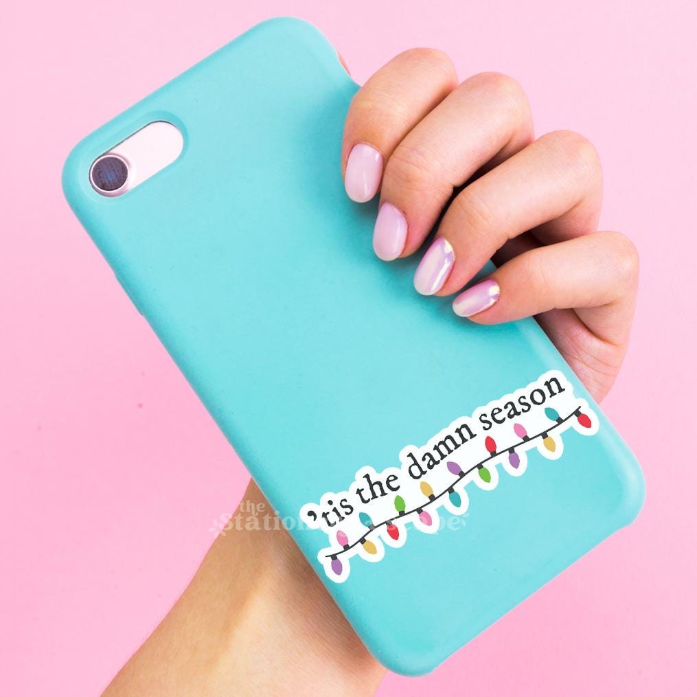 Turquoise phone case with Christmas lights and text held by a hand on a pink background