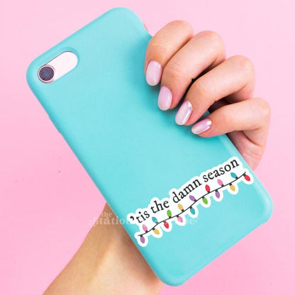 Turquoise phone case with Christmas lights and text held by a hand on a pink background