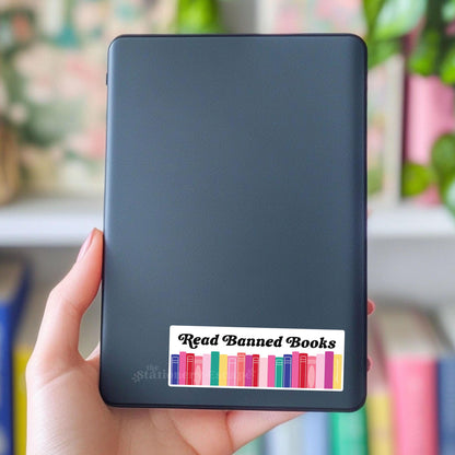 Black e-reader with 'Read Banned Books' sticker held by a hand, blurred background