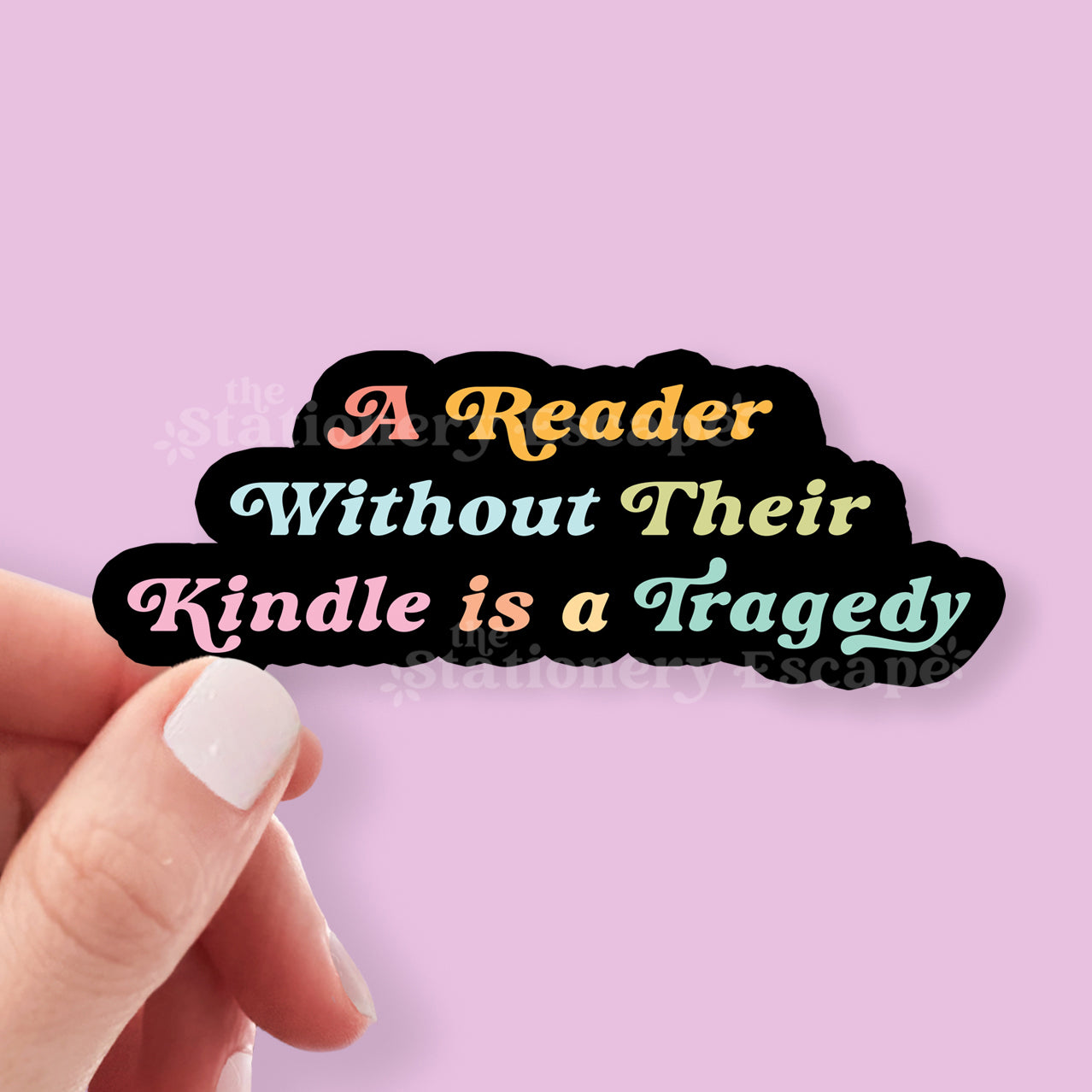 Sticker with text 'A Reader Without Their Kindle is a Tragedy' held by a hand against a pink background