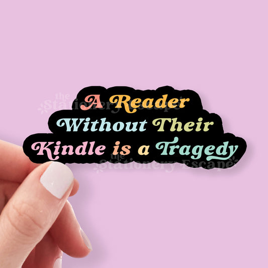 Sticker with text 'A Reader Without Their Kindle is a Tragedy' held by a hand against a pink background