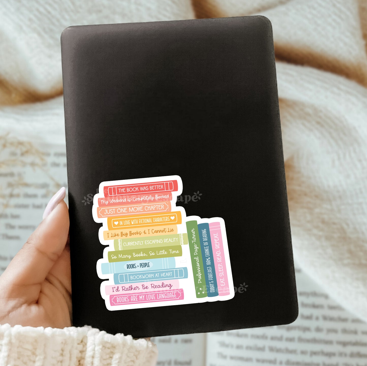 Black Kindle case with colorful book stack sticker design held by a hand on a textured surface