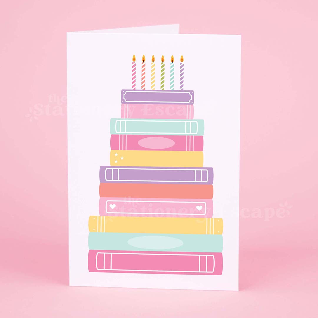 Colorful birthday card featuring a "birthday cake" made from pastel colored stacked books on a pink background