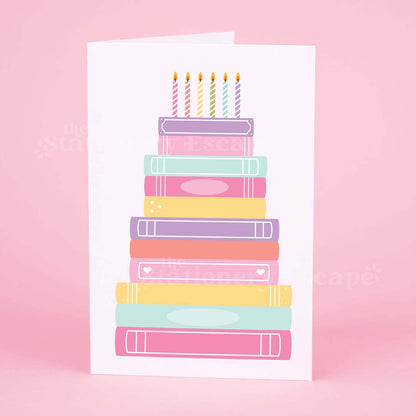 Colorful birthday card featuring a "birthday cake" made from pastel colored stacked books on a pink background