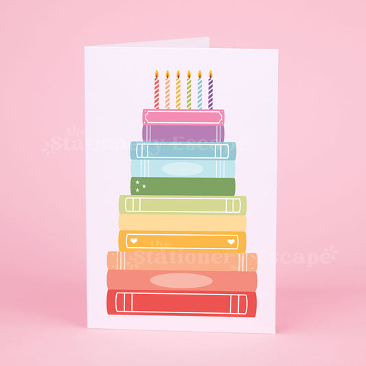 Colorful birthday card featuring a "birthday cake" made from rainbow stacked books on a pink background