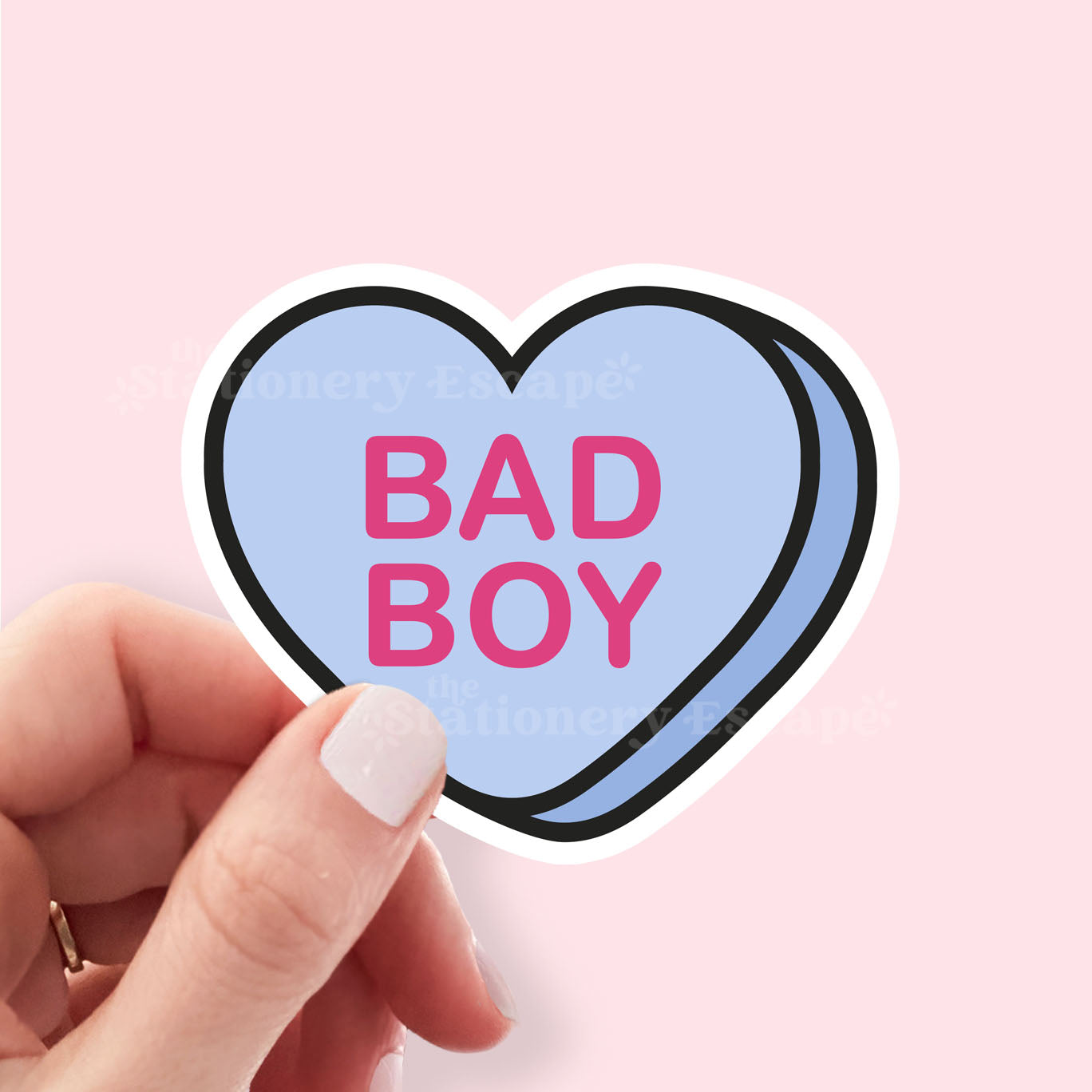 Heart-shaped sticker with 'BAD BOY' text held by a hand against a pink background