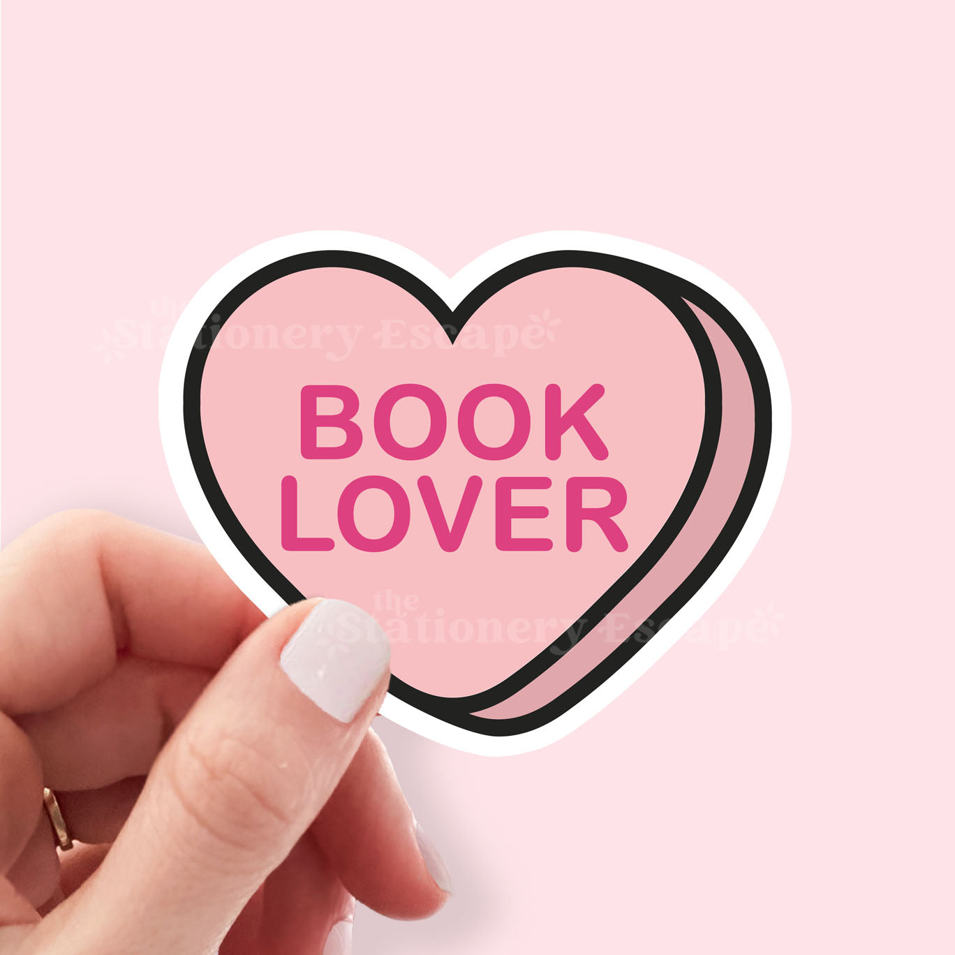 Heart-shaped sticker with 'BOOK LOVER' text held by a hand on a pink background