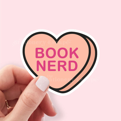 Heart-shaped sticker with 'BOOK NERD' text held by a hand on a pink background