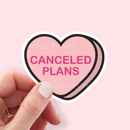 Heart-shaped sticker with 'Canceled Plans' text held by a hand on a pink background