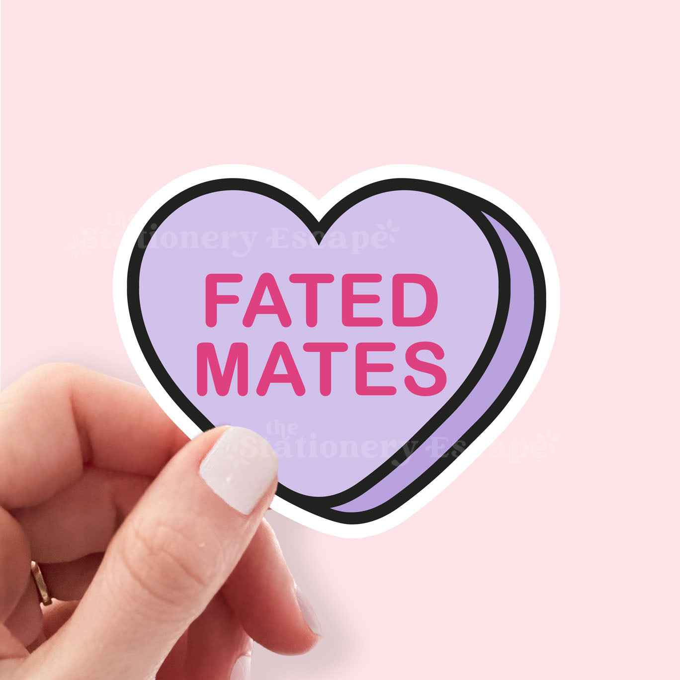 Heart-shaped sticker with 'FATED MATES' text held by a hand against a pink background