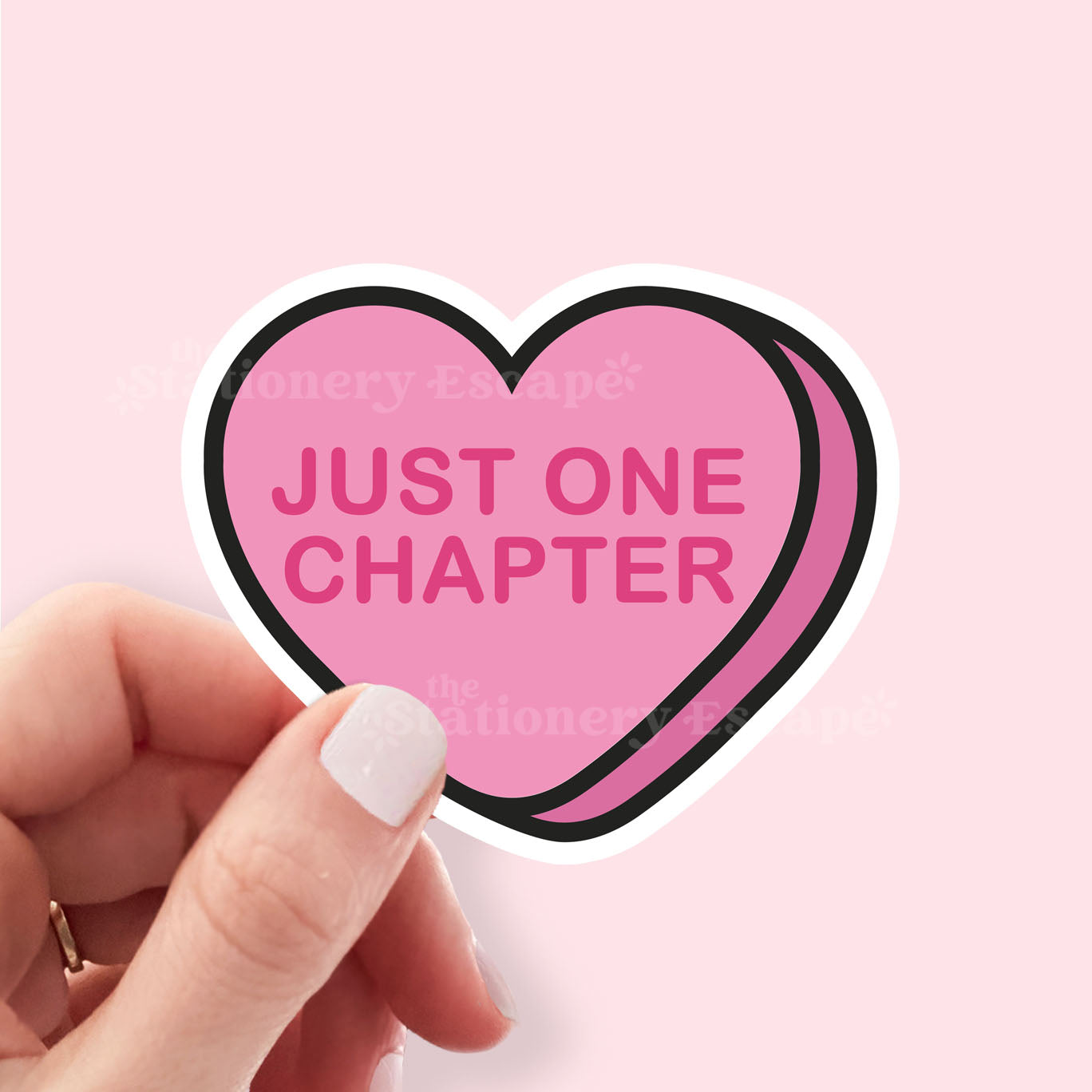 Heart-shaped sticker with 'JUST ONE CHAPTER' text held by a hand against a pink background