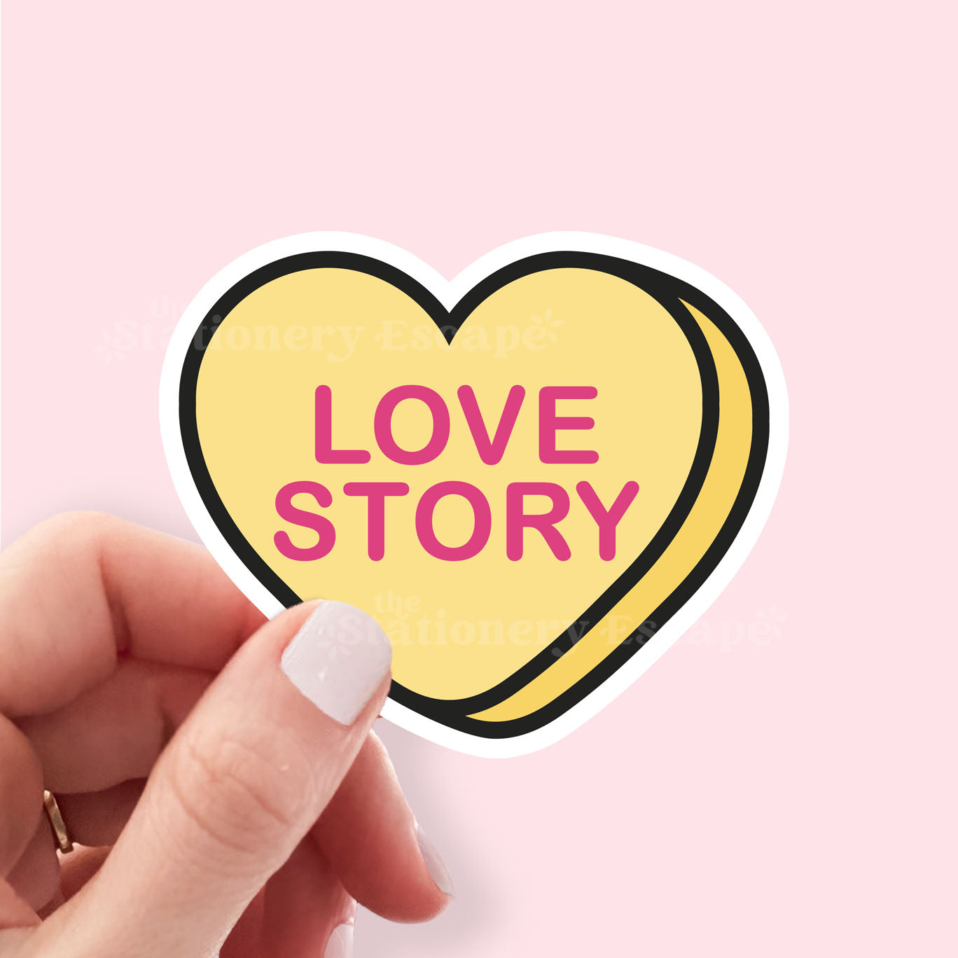 Heart-shaped sticker with 'LOVE STORY' text held by a hand on a pink background