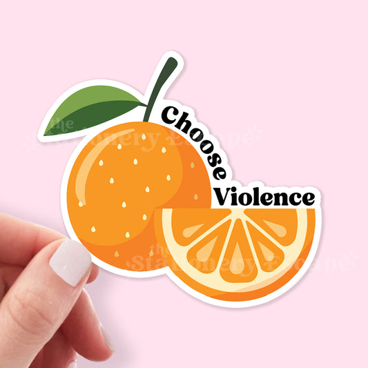 Sticker of an orange with 'Choose Violence' text held by a hand on a pink background