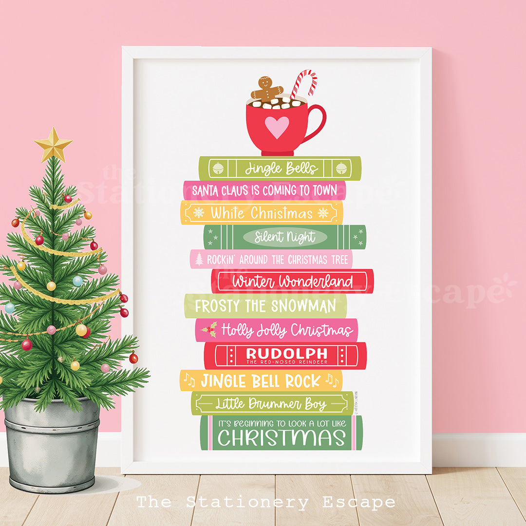 Framed Christmas-themed book stack print with holiday songs as titles and a small Christmas tree on a pink wall.