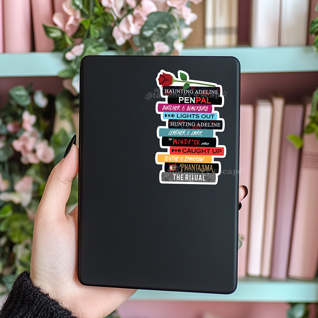 Black Kindle case with dark romance book stack sticker held by a hand against a blurred floral background