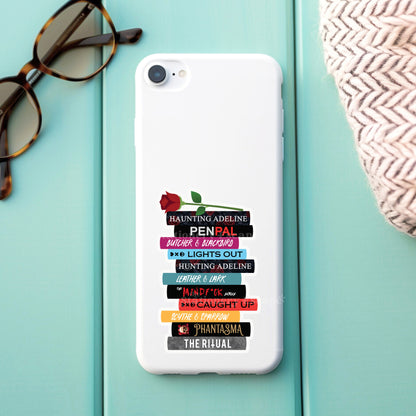 Phone case with dark romance book stack sticker on a light blue surface with sunglasses and a woven bag.