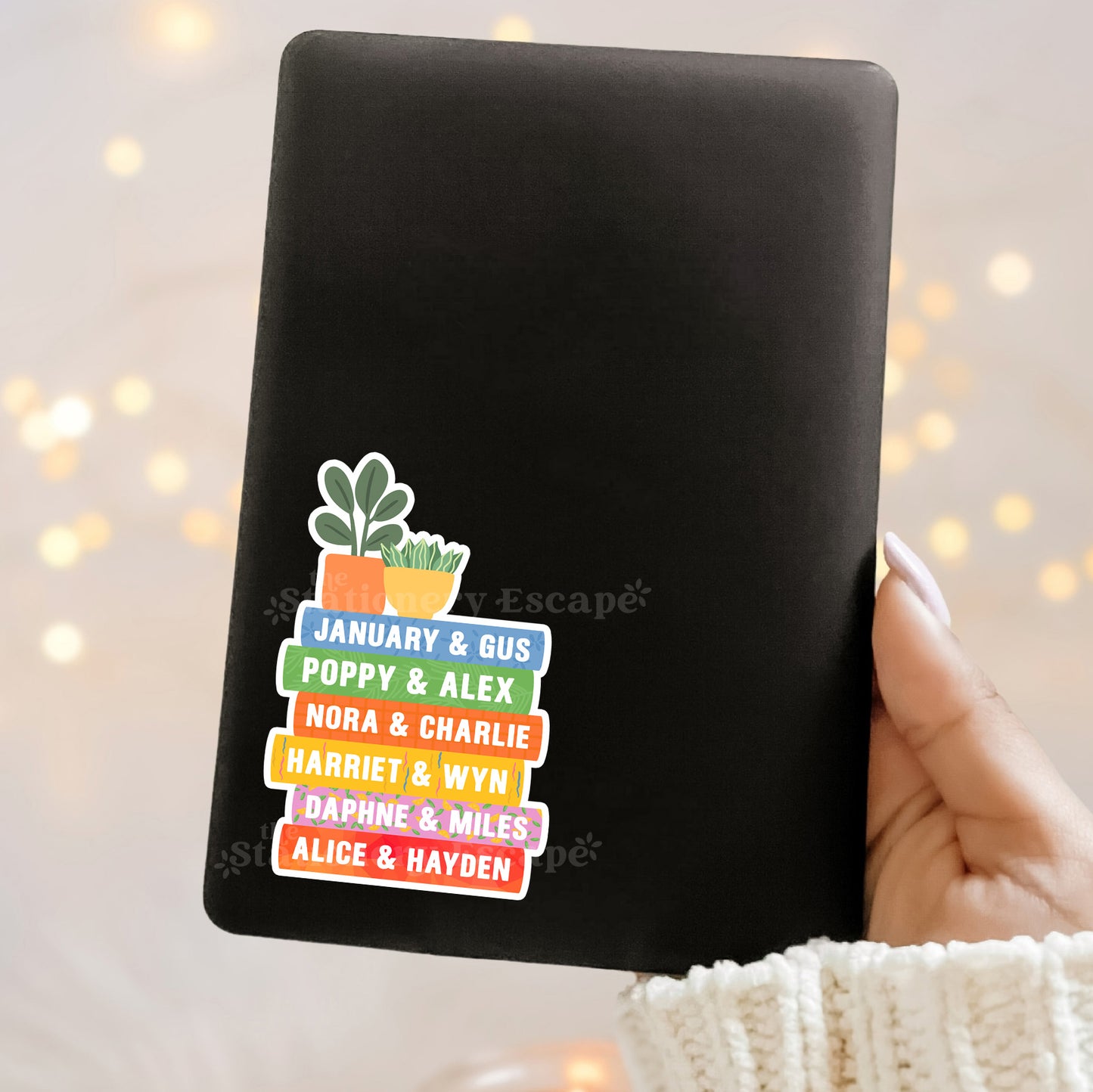 Black Kindle case with colorful Emily Henry book stack and plant design sticker on a blurred light background