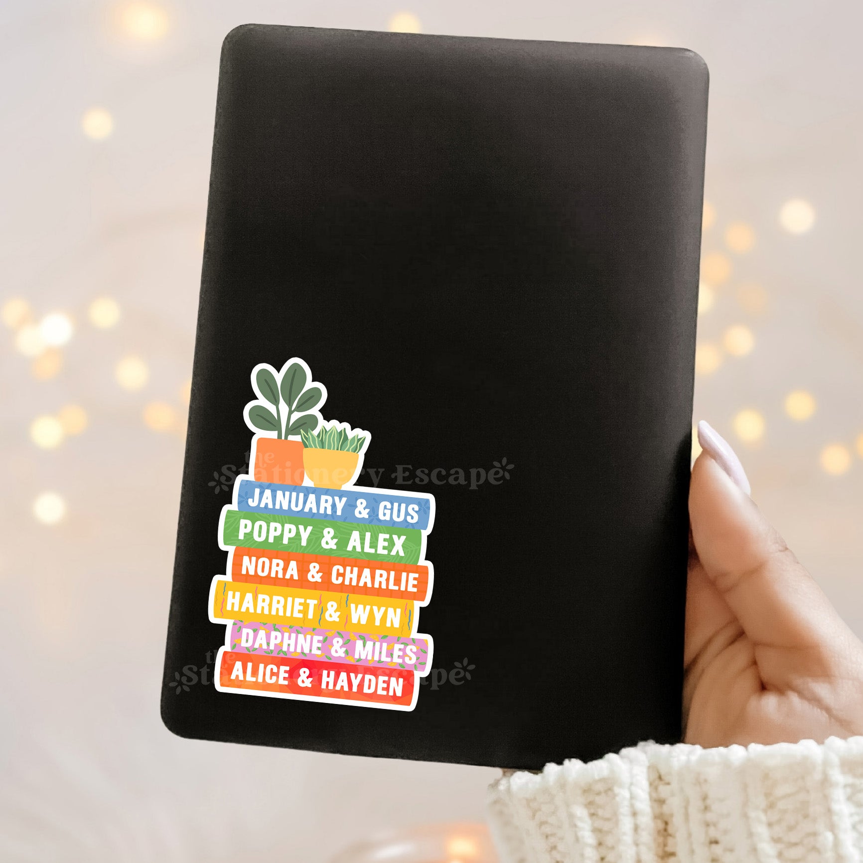Black Kindle case with colorful Emily Henry book stack and plant design sticker on a blurred light background
