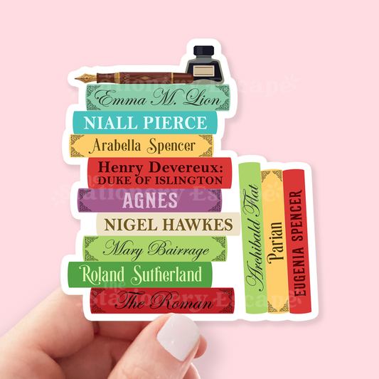 A hand holds a die-cut sticker shaped like a stack of colorful books, each labeled with an Emma M. Lion Character, against a soft pink background.