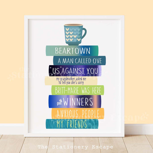 Framed colorful book stack art print featuring the spines and titles of literary novels by Fredrik Backman. The book stack is topped by a heart-decorated mug of coffee.