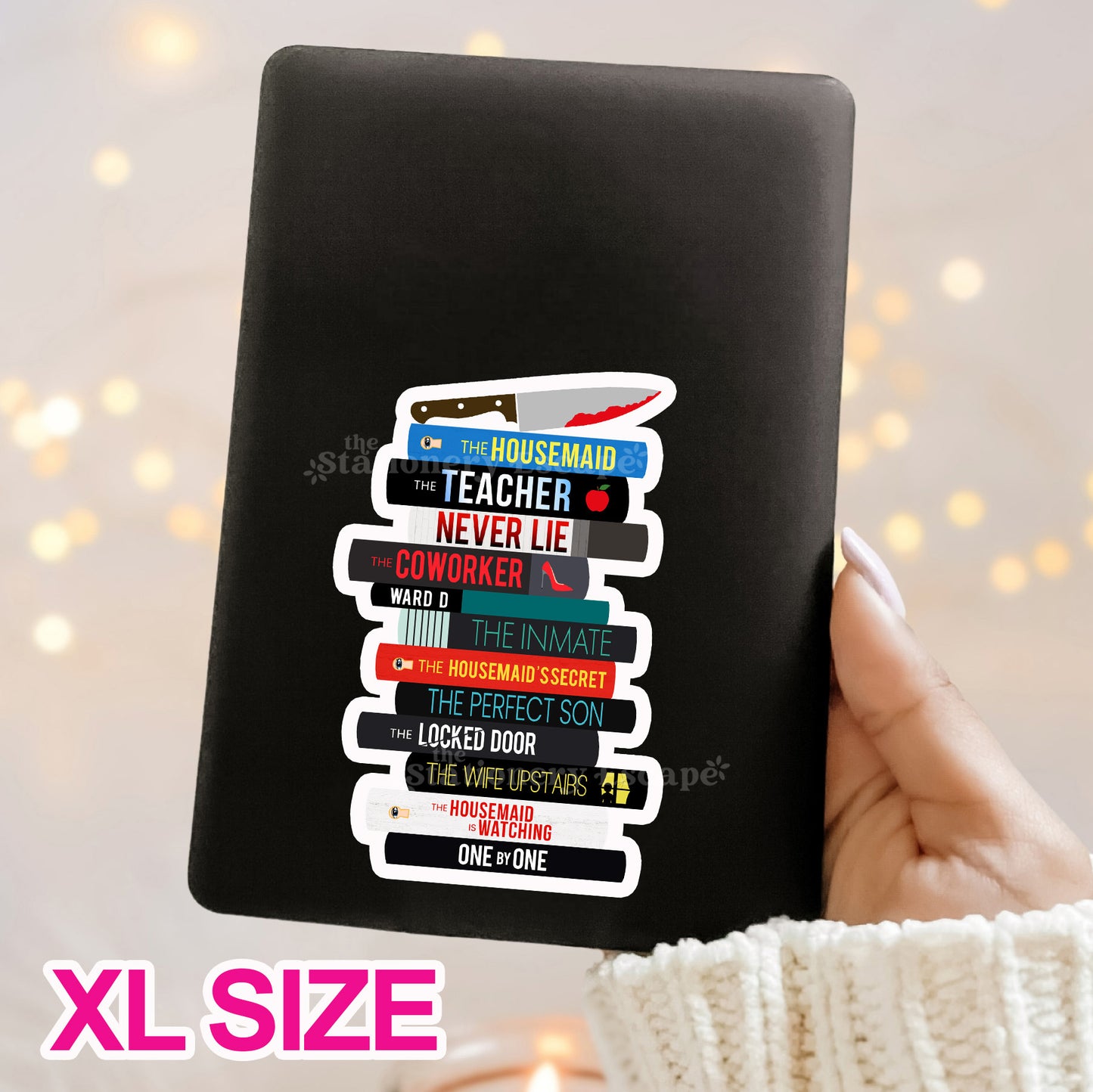 Black Kindle case with a colorful Freida McFadden book stack sticker held by a hand against a blurred light background