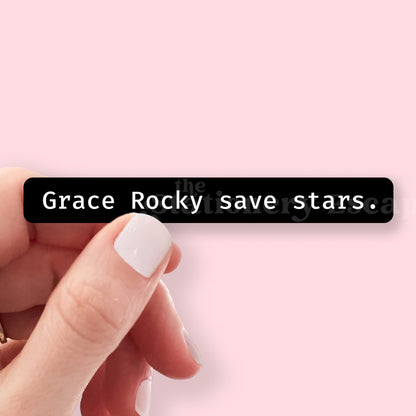 Hand holding a black bar with text 'Grace Rocky save stars.' on a pink background