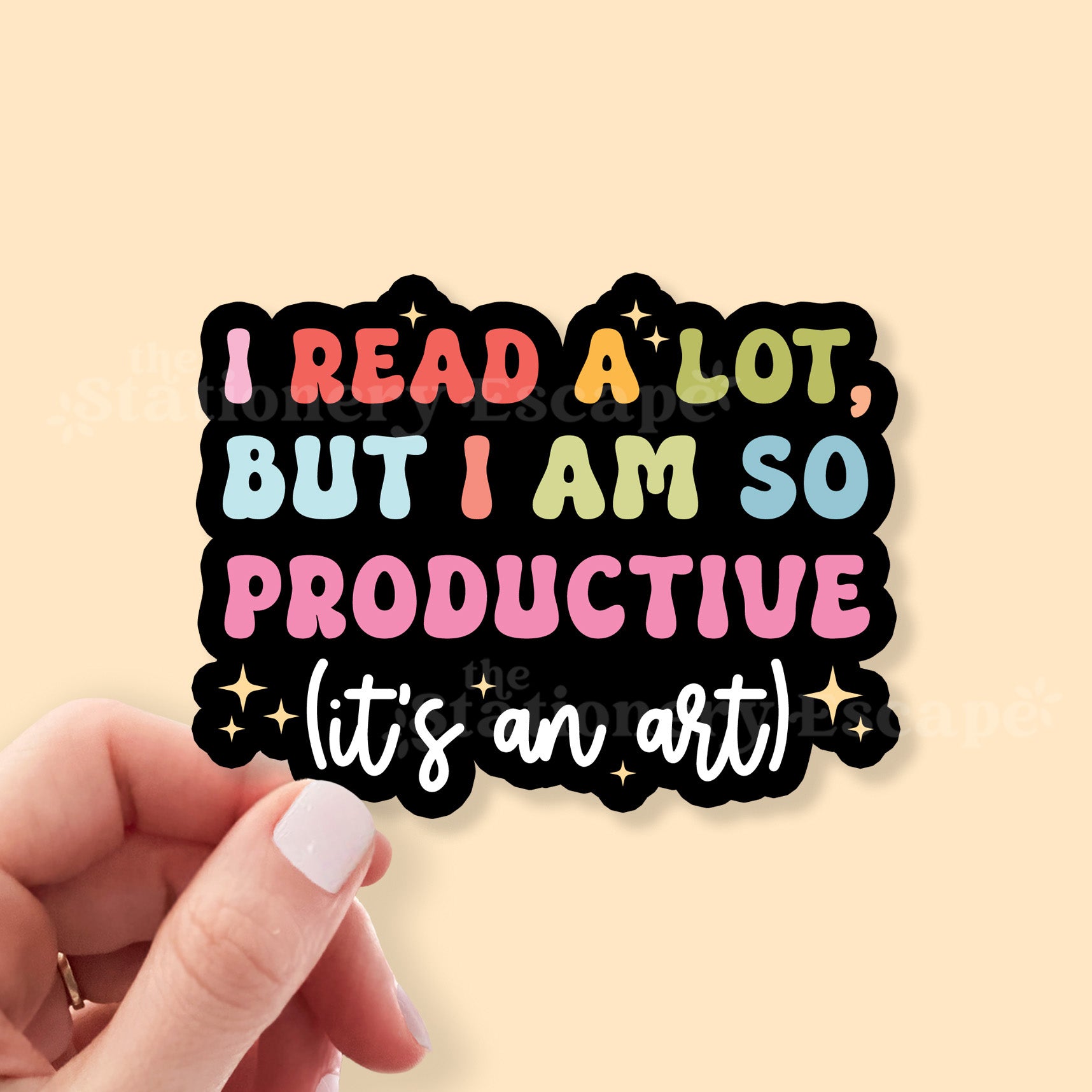 Colorful sticker with text 'I read a lot, but I am so productive (it's an art)' held by a hand on a beige background