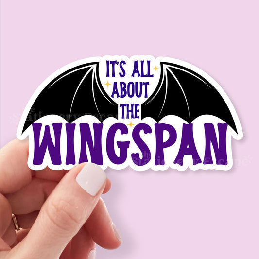 Sticker with bat wings and 'It's All About The Wingspan' text held by a hand against a light purple background
