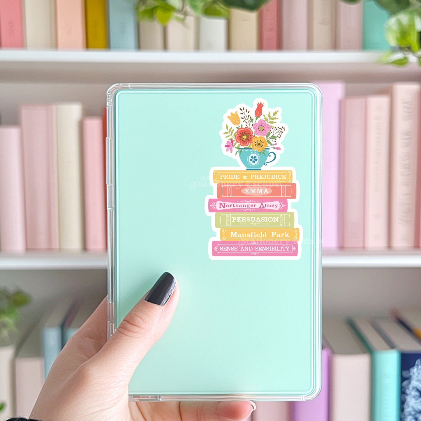 Kindle with a colorful Jane Austen bookshelf design sticker held in front of a bookshelf background
