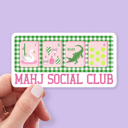 Sticker with 'MAHJ SOCIAL CLUB' design held by a hand against a purple background