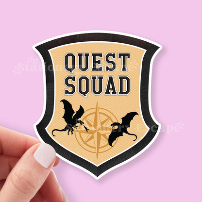 Shield-shaped sticker with 'Quest Squad' text and dragons on a pink background