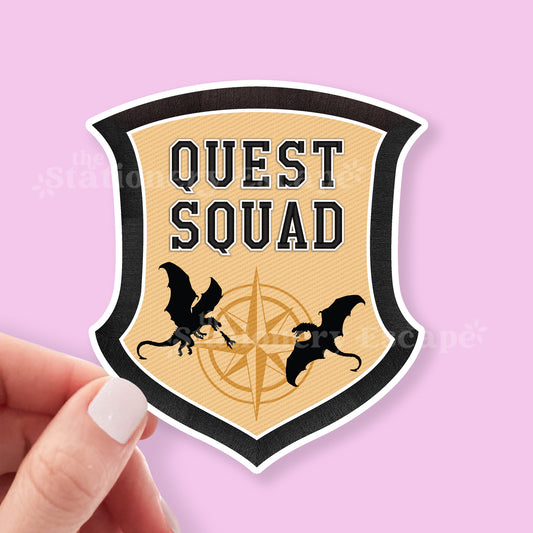 Shield-shaped sticker with 'Quest Squad' text and dragons on a pink background