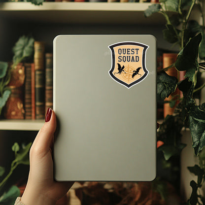 Hand holding a tablet with 'Quest Squad' sticker in front of a bookshelf