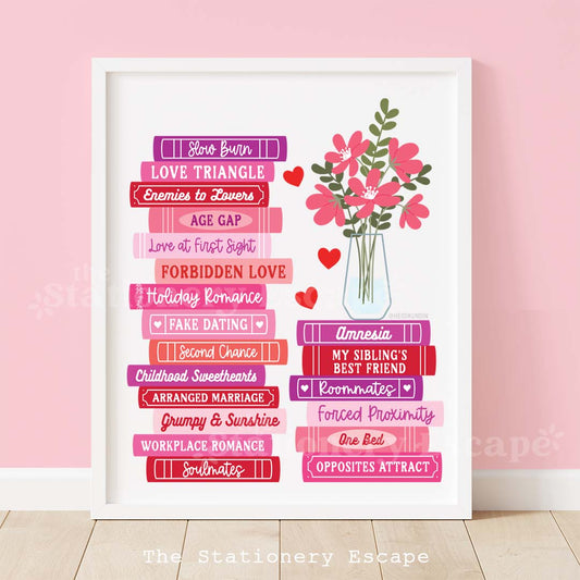 Framed romance-themed book stack print with titles featuring romance tropes such as One Bed and Fake Dating on pink, red, and purple book spines.