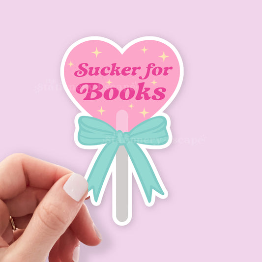 Heart-shaped lollipop sticker with 'Sucker for Books' text on a pink background