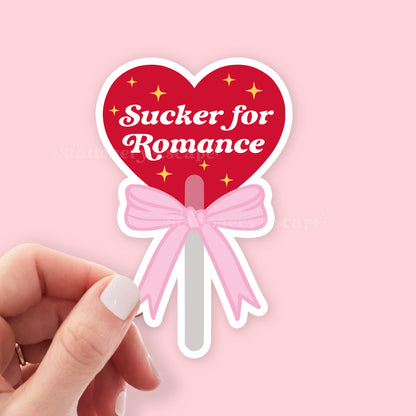 Heart-shaped lollipop sticker with 'Sucker for Romance' text on a pink background