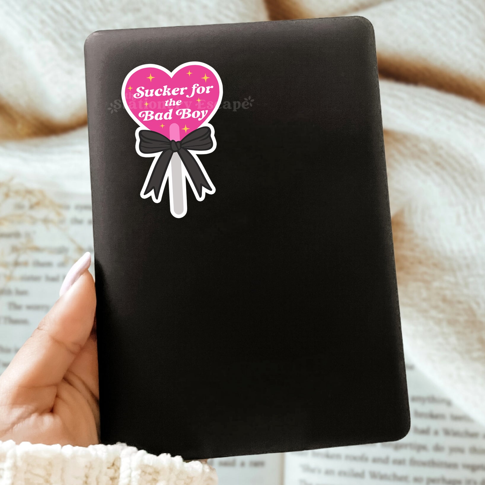 Black Kindle with a pink heart-shaped lollipop sticker and "Sucker for the Bad Boy" text on a textured surface