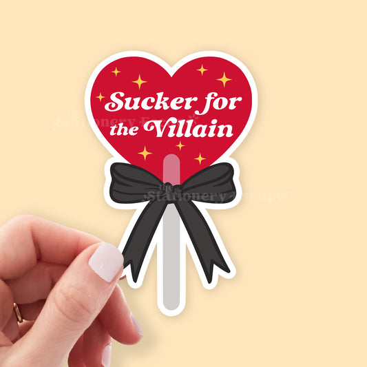 Heart-shaped lollipop sticker with 'Sucker for the Villain' text on a beige background