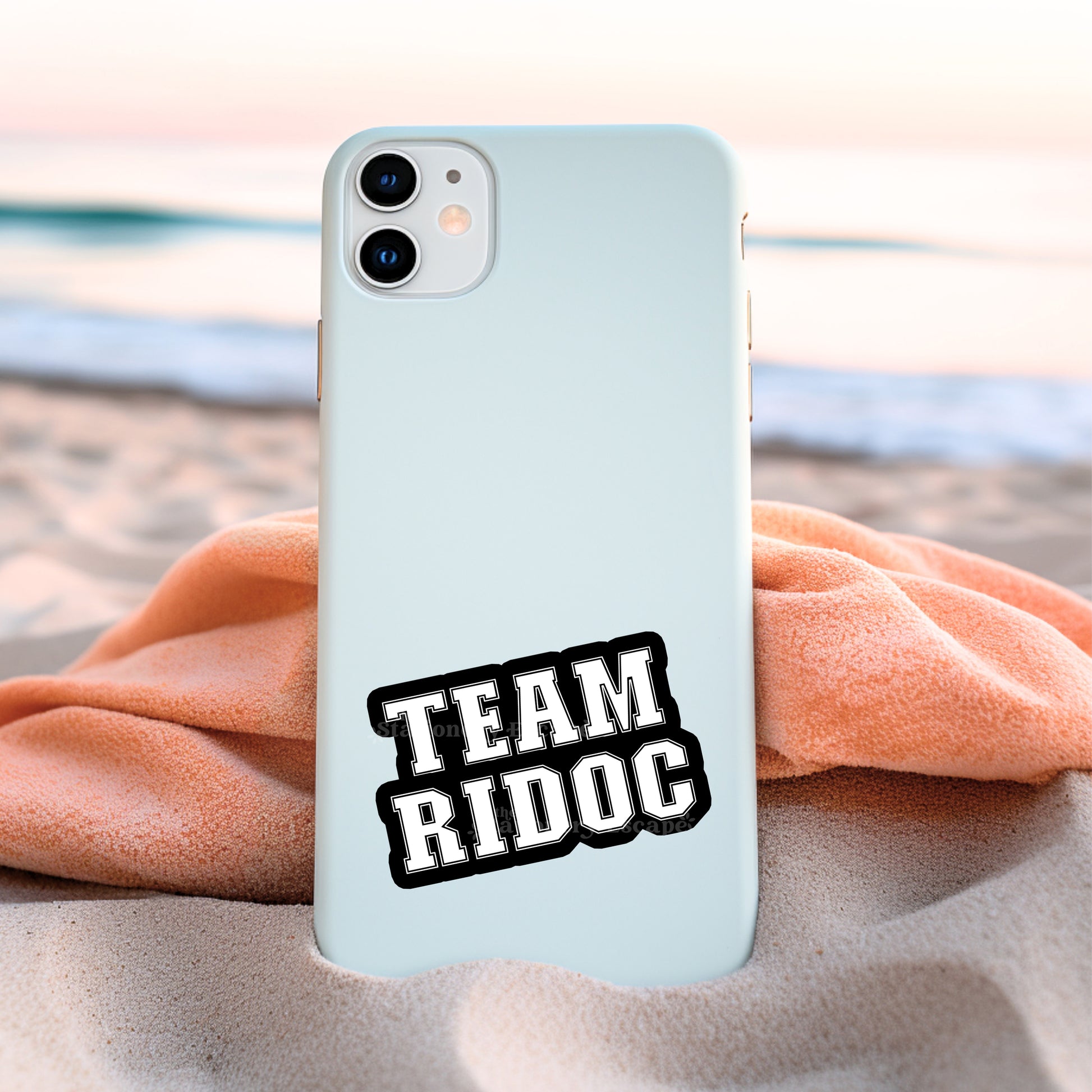 Phone case with 'TEAM RIDOC' sticker on a beach setting