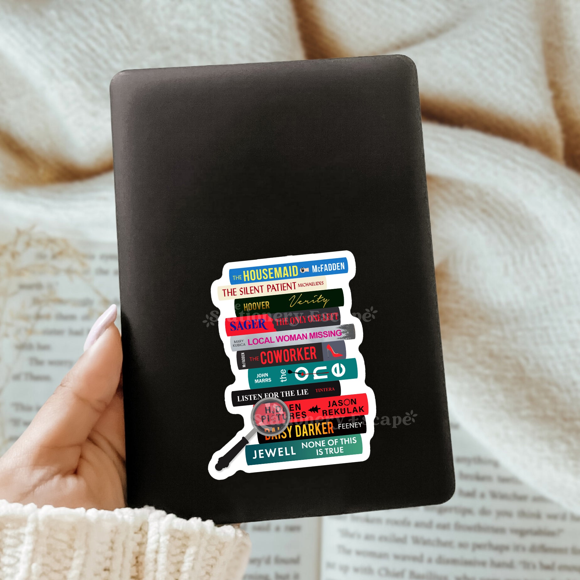 Black Kindle case with colorful book stack sticker held by a hand on a textured surface