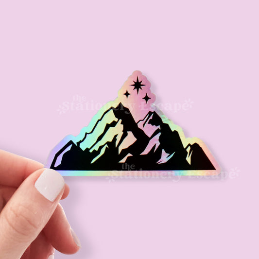 Holographic mountain sticker held by a hand against a light purple background
