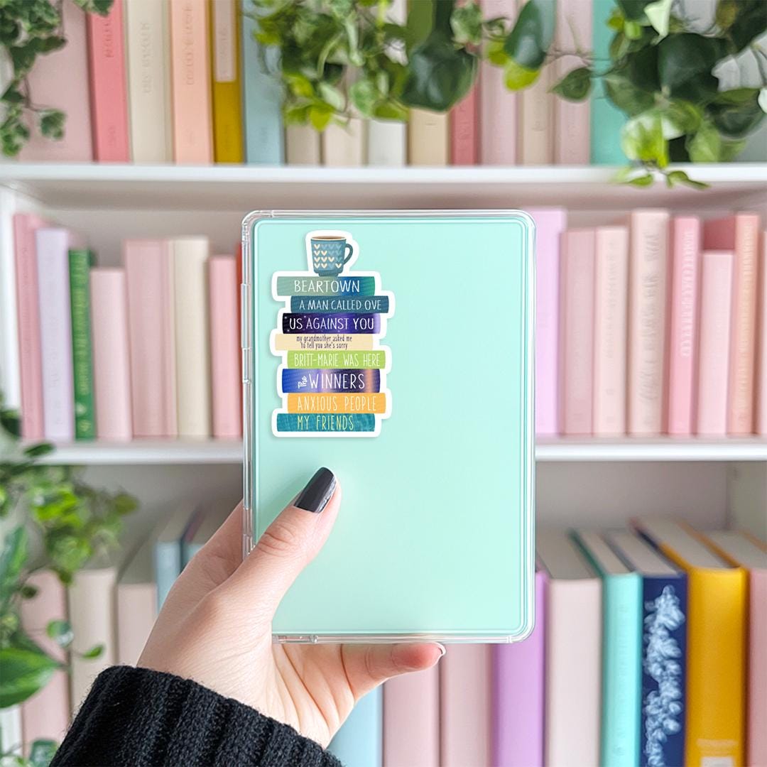 Hand holding a Kindle with a colorful case and Fredrik Backman book stack sticker in front of a bookshelf