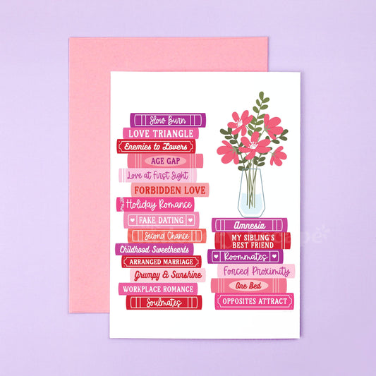 Card with romance tropes as book title text and floral design on a pink envelope against a light purple background