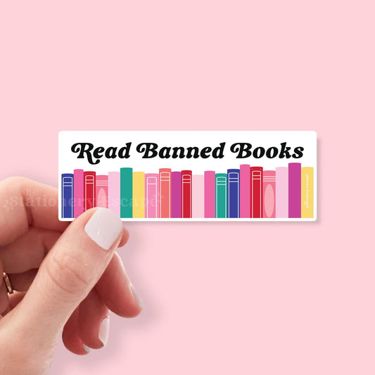 Sticker with 'Read Banned Books' text and colorful book illustrations held by a hand on a pink background.