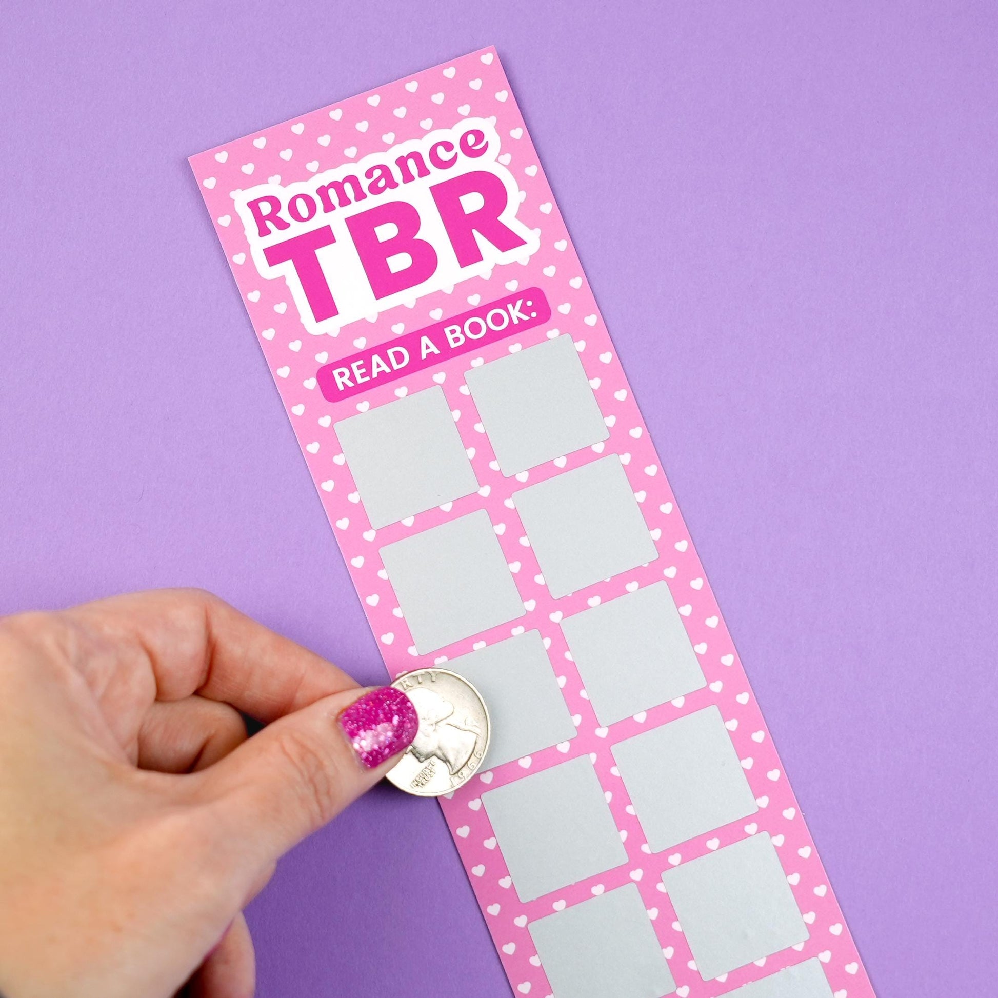 Pink 'Romance TBR' scratch-off bookmark with heart patterns on a purple background